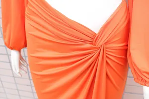 Detailaufnahme eines lebendigen orangefarbenen Bodycon-Kleides mit Knotendetail und Raffung.