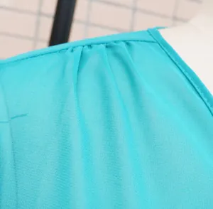 Macro view showing the pleated shoulder detail and fabric texture of a turquoise chiffon beach dress