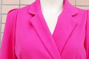 Dettaglio ravvicinato del colletto a rever e della spalla di un abito blazer fucsia.