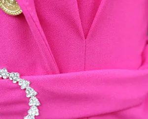 Dettaglio dell'abito blazer rosa che evidenzia la fibbia di strass e la trama del tessuto