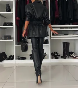 Rückansicht einer Frau in einem schicken schwarzen Trenchcoat aus Kunstleder im Kleiderschrank