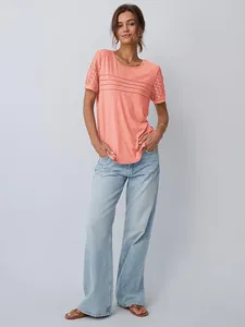 Modella indossa t-shirt rosa corallo con maniche in pizzo e jeans azzurro chiaro