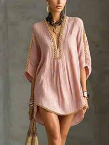 Close-up of the V-neckline and golden woven trim detail on a pink pleated vacation dress