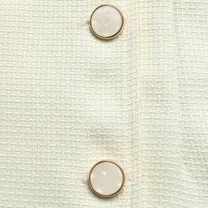 Detailed macro view of cream tweed fabric featuring elegant gold-rimmed pearlescent buttons.