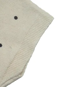 Detailansicht eines cremefarbenen Strickpullovers mit weichem schwarzen Punktmuster.