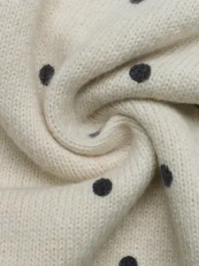 Nahaufnahme von weichem, cremefarbenem Strickstoff mit eleganten schwarzen Punkten Mustern