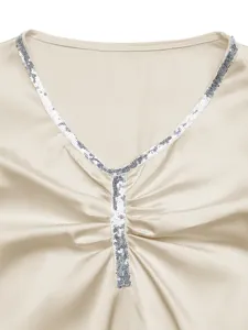 Detail van zilveren pailletten en geplooide satijnstof op een bodysuit met V-hals.