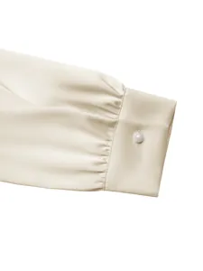 Detail van een elegante champagne satijnen mouwboord met plooien en een parelknoop.