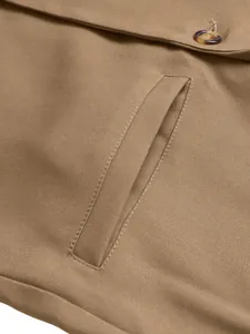 Detailopname van een bruine blazer met een paspelzak en een knoopsluiting detail.