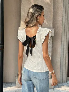 Detailansicht des rückenfreien Designs mit schwarzer Schleife auf weißem Stricktop.