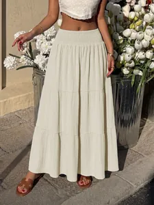 Detail view of the smocked high waist on a cream tiered A-line maxi skirt outdoors