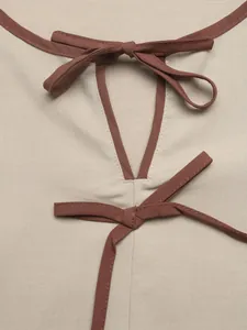 Detail einer beige Bluse mit braunen Kontrastpaspeln und zwei Schleifenakzenten.