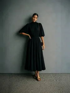 Elegante zwarte jurk met opstaande kraag, pofmouwen en een geplooide rok