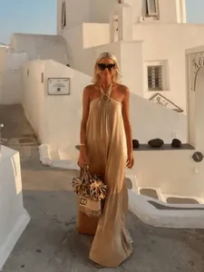 Elegantes blondes Model in einem goldenen Neckholder-Maxikleid für den Urlaub auf Santorini