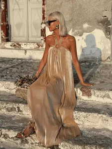 Model in einem champagnerfarbenen, metallischen Halter-Maxikleid auf Steinstufen