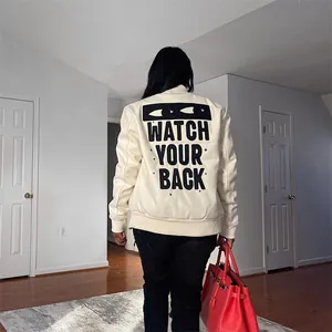 Back view of an apricot bomber jacket with "WATCH YOUR BACK" print and eye graphic