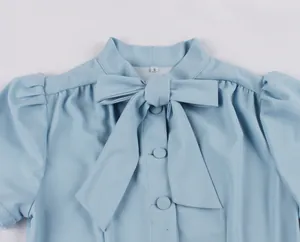 Close-up of light blue dress neck with large decorative bow tie and buttons.