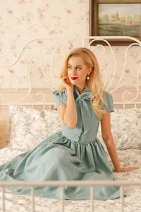 Elegant vintage dusty blue dress with bow tie collar and swing skirt in bedroom setting.