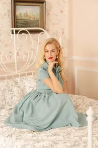 Elegant light blue tie-neck flared midi dress worn by a model in a vintage bedroom.