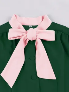 Close-up detail of a dark green dress featuring a prominent pink bow and button collar