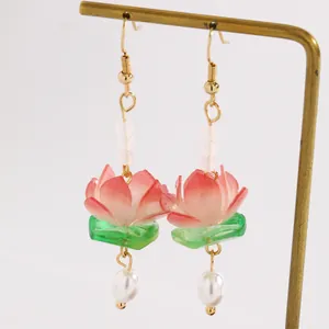 Close-up of pink gradient lotus flower earrings with white pearl drops on brass stand