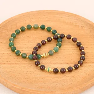 Detailed macro view of green and garnet semi-precious stone beaded bracelets on a wooden tray.