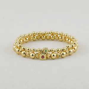 Detailed view of two gold-beaded elastic bracelets with red and green gemstone charms.