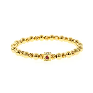 Detail view of a handmade gold beaded elastic bracelet featuring red tourmaline