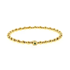 Detailed macro view of a gold beaded bracelet with a colorful gemstone square bead