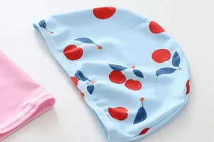 Detail view of blue children's swimming cap with cherry pattern and pink fabric