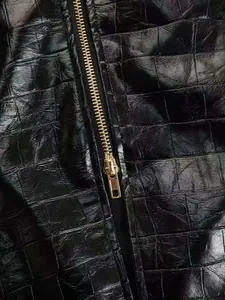 Macro detail of glossy black crocodile embossed faux leather with gold zipper