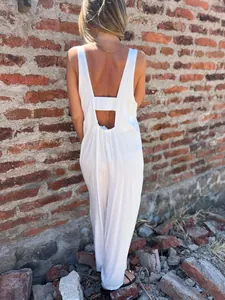 Back view of a loose white sleeveless jumpsuit for women against a brick wall background.