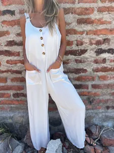 Front view of white loose suspender jumpsuit featuring brown buttons and front pockets.