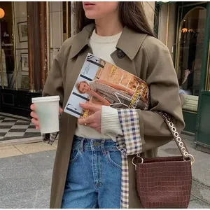 Detail of long brown lapel trench coat with checkered cuff lining in street style.