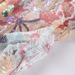Macro view of intricate floral embroidery and colorful sequins on delicate mesh fabric.