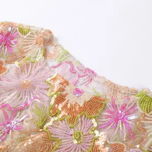 Detailed macro view of colorful floral embroidery and sparkling sequins on mesh fabric.