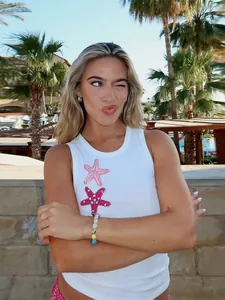 Blondes Model trägt ein weißes Tanktop mit Seestern-Stickerei im Sommerresort