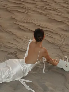 Elegantes weißes rückenfreies Satin-Maxikleid im Sand, ideal für einen luxuriösen Urlaub.