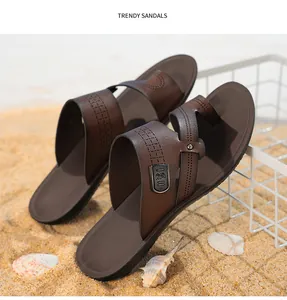 Detaillierte Nahaufnahme modischer brauner Herren-Sandalen auf Sand mit Muscheln