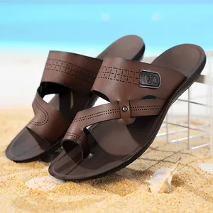 Bequeme braune Herren-Pantoletten mit Zehenschlaufe auf einem Strand-Sandhintergrund