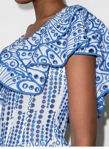 Nahaufnahme eines eleganten weiß-blauen Bestickte-Ösen-Kleids mit Rüschen-Schulter-Detail.
