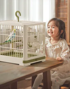 Bambina che osserva un pappagallo blu in una gabbia per uccelli portatile in plastica