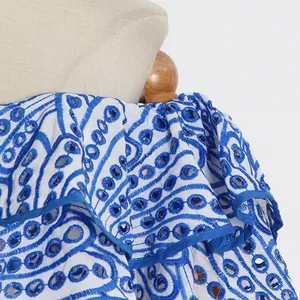 Nahaufnahme der komplizierten blauen Ösenstickerei auf einem eleganten weißen Kleid.
