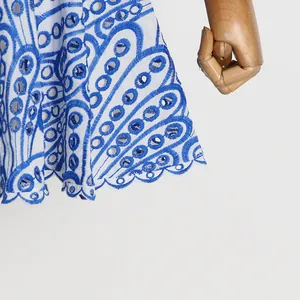 Nahaufnahme eines weißen Kleides mit blauer Lochstickerei und gewelltem Saumdetail.