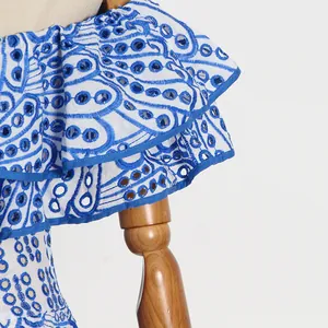 Detailaufnahme der blauen Stickerei und der zarten Lochstickerei am weißen Rüschenkleid