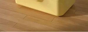 Detalle de la esquina del arenero amarillo antisalpicaduras sobre suelo de madera