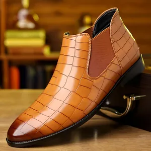 Close-up detail of tan crocodile-patterned men's Chelsea boot on wooden desk