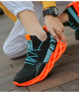 Gros plan de baskets à lame noires et orange respirantes pour hommes dans la rue.