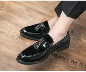 Detailed view of men's black patent leather loafers with tassels on a wooden floor.