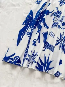 Detailed view of the vibrant blue tropical palm and bird print on white summer dress fabric